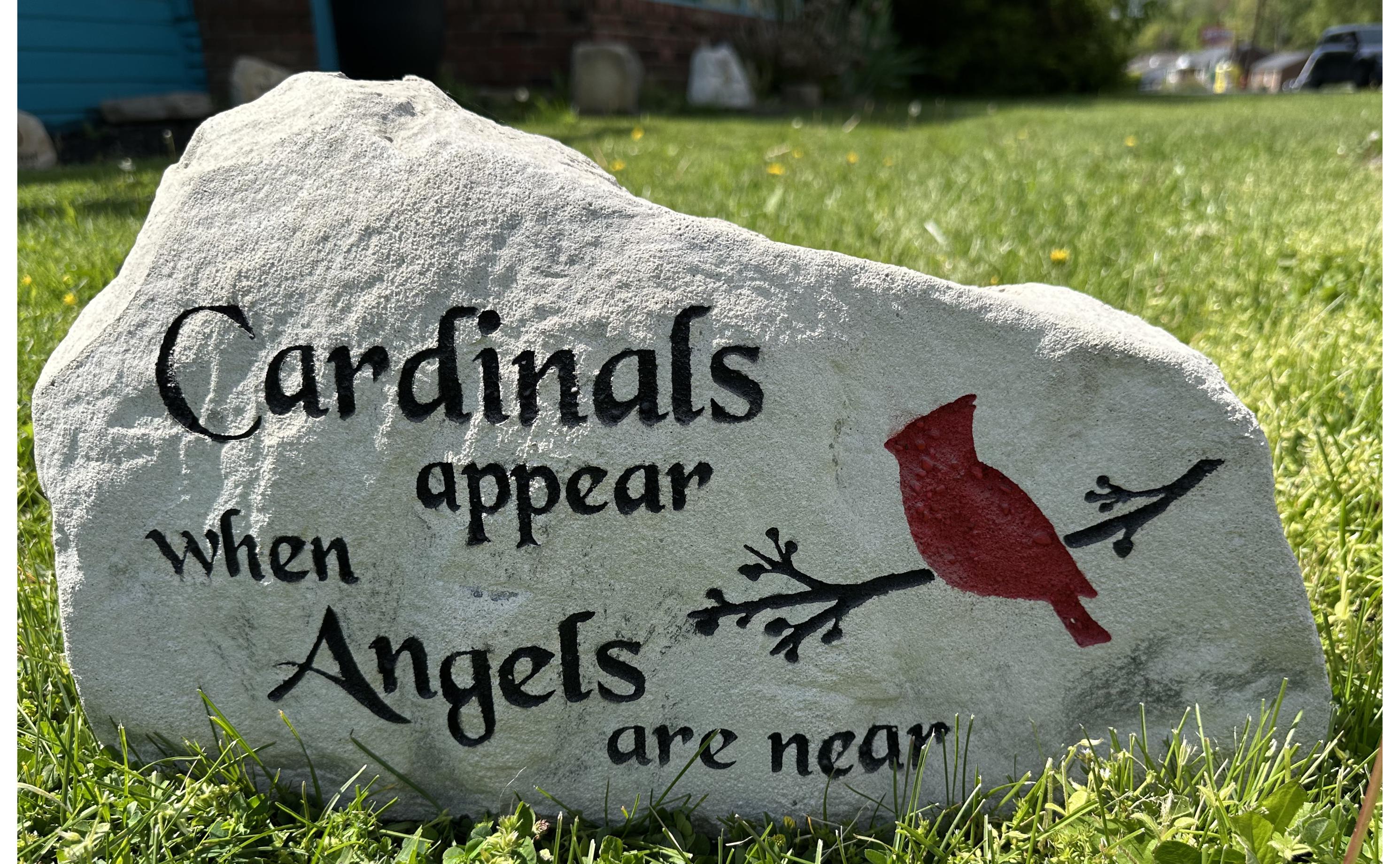 A large, grey landscape stone with an irregular, rounded shape. The left hand side of the stone is slightly taller than the right size of the stone. The stone sits upright giving a nice face to engrave upon. The stone has a rustic, handcrafted appearance with natural texture and subtle color variations. This stone has the text Cardinals appear when angels are near along with a cardinal on a tree branch. The text & branch are painted black, the cardinal is a bold red color.