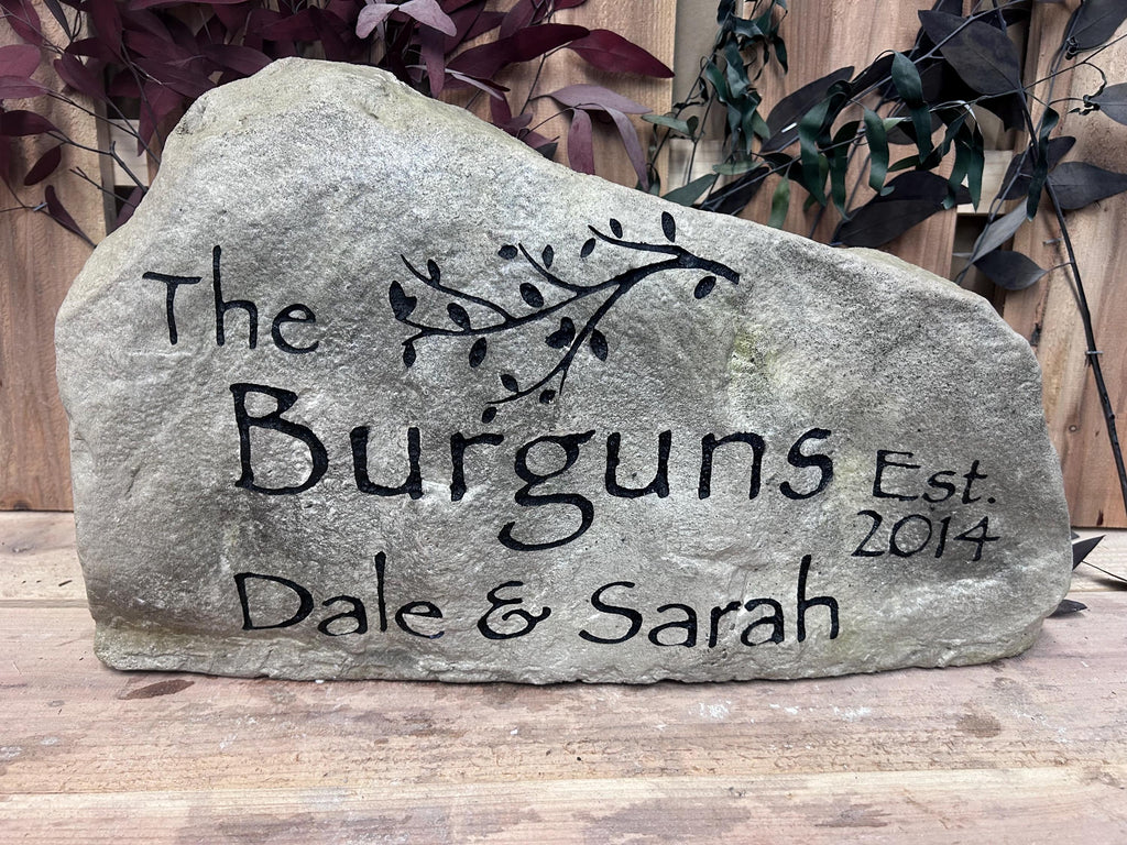 A large, grey landscape stone with an irregular, rounded shape. The left hand side of the stone is slightly taller than the right size of the stone. The stone sits upright giving a nice face to engrave upon. The stone has a rustic, handcrafted appearance with natural texture and subtle color variations. This stone has a family name on it and an established date. It also has a tree branch graphic. The engraved portions are painted black.